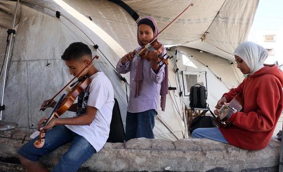 Un niño y dos niñas tocan música dentro de una tienda de campaña en Gaza.